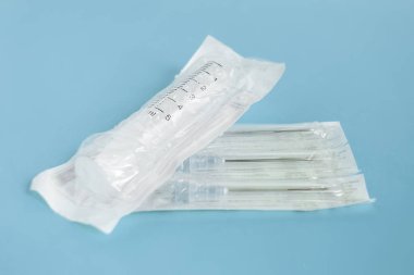 Bir tek kullanımlık tıbbi şırınga ve iğne enjeksiyon mavi arka plan, bireysel Steril ambalaj, her öğe için Kapat.