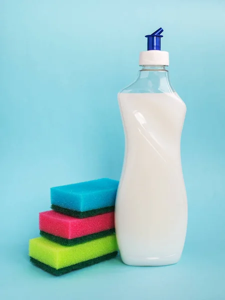 在蓝色背景上 用白色洗碗液和三种不同颜色的泡沫海绵装瓶 厨房洗涤剂 家用化学品 — 图库照片
