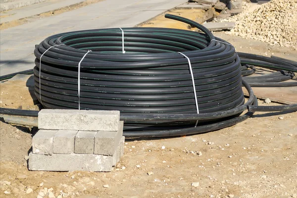 新的黑色电缆线圈或塑料管道软管 用于铺设在道路工程工地的沟里 修复人行道 更换城市街道上的电缆和管道 — 图库照片