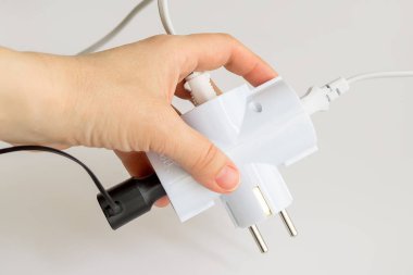 Kadın el beyaz elektrik splitter içine beyaz bir arka plan üzerinde ek ağaç fişleri ile tutarak. Splitter aynı anda üç elektrikli ev aletleri geçiş yapmak için. Elektrik splitter ve fiş.