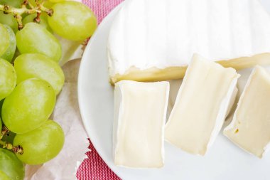 Pembe masa örtüsü üzerinde beyaz plaka ve tatlı yeşil üzüm üzerinde lezzetli peynir Camembert parçaları. Yenilebilir beyaz kalıp ile kaplı yumuşak peynir.