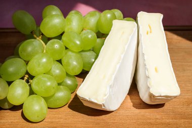 Kahverengi ahşap arka plan üzerinde penceresinden bir güneş ışığı altında lezzetli peynir Camembert ve tatlı yeşil üzüm parçaları. Yenilebilir beyaz kalıp ile kaplı yumuşak peynir.