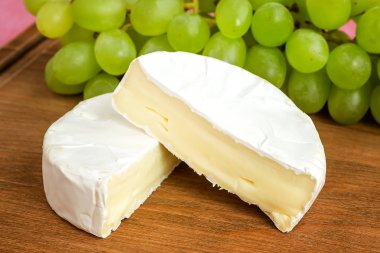 Kahverengi ahşap kesme tahtasında lezzetli peynir Camembert ve tatlı yeşil üzüm parçaları. Yenilebilir beyaz kalıp ile kaplı yumuşak peynir.