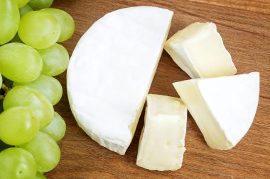 Kahverengi ahşap kesme tahtasında lezzetli peynir Camembert ve tatlı yeşil üzüm parçaları. Yenilebilir beyaz kalıp ile kaplı yumuşak peynir.