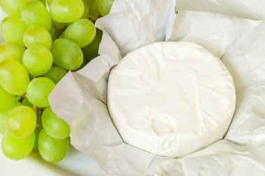Tüm baş Camembert sadece açık kağıt paketi ve beyaz plaka tatlı yeşil üzüm demet. Yumuşak peynir yenilebilir beyaz kalıp ile kaplıdır. Üst görünüm.