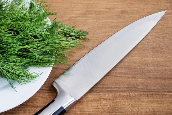 Sharp professional chef knife on a bunch of fresh green dill