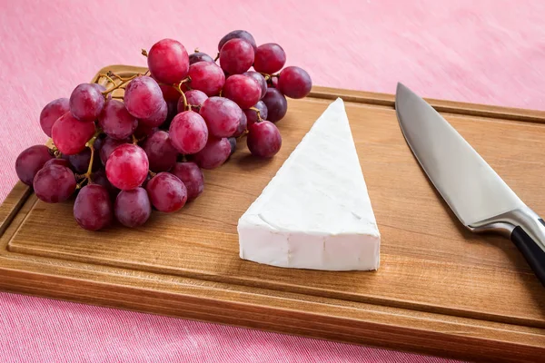 Háromszögletű darab Brie sajt, vörös édes szőlő és egy szakács kés — Stock Fotó