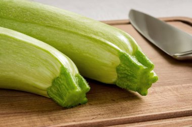 Kahverengi ahşap kesme tahtası üzerinde iki taze yeşil kabak ve profesyonel şef bıçak