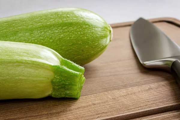 Deux courgettes vertes fraîches et un couteau de chef professionnel sur une planche à découper en bois marron — Photo