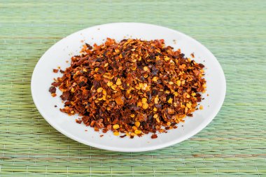 Yeşil bir masa mat üzerinde beyaz bir tabak üzerinde kurutulmuş ve cruched kırmızı acı biber