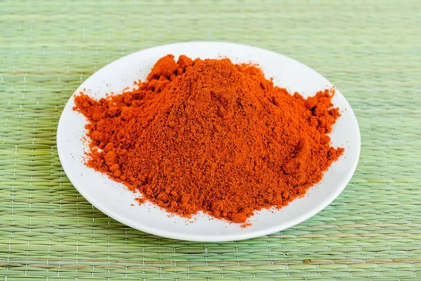 A heap of dry red paprika powder on a white saucer on a green table mat