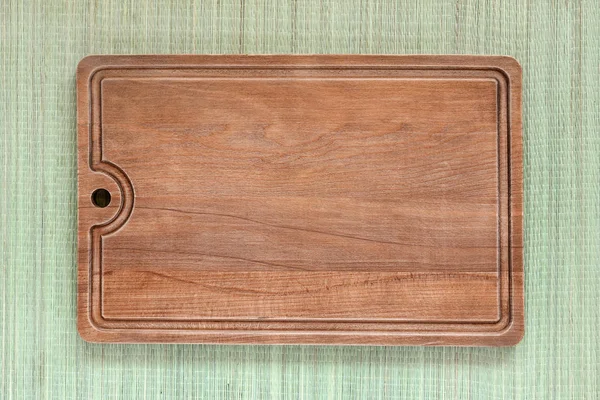 Brown wooden cutting board on a background of a rough green mat ma — Stock Photo, Image