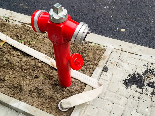 Hidrante de fuego rojo con un sello abierto y una larga manguera de fuego blanca — Foto de Stock
