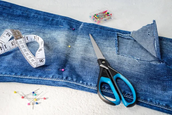 Gefaltet in halbblaue Jeans mit großem Loch, Nähnadeln, Maßband und Schere — Stockfoto