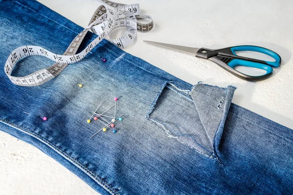 Plegado en pantalones vaqueros medio azules con un agujero, alfileres de costura, cinta adhesiva y tijeras — Foto de Stock
