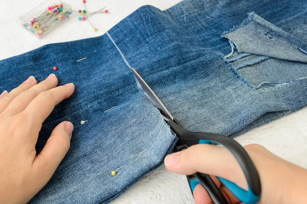 Woman hand holdig a scissors and cutting out a jeans pant legs with hole — Stock Photo, Image