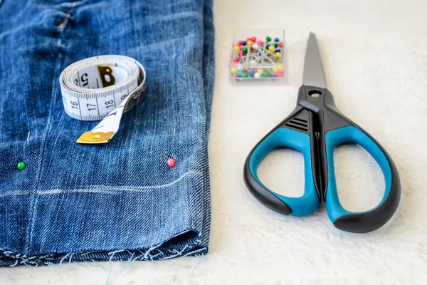 Pantalones cortos de mezclilla azul, alfileres de costura, rollo de cinta adhesiva y tijeras — Foto de Stock