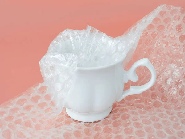 Weiße elegante Teetasse halb verpackt mit transparenter Luftpolsterfolie — Stockfoto