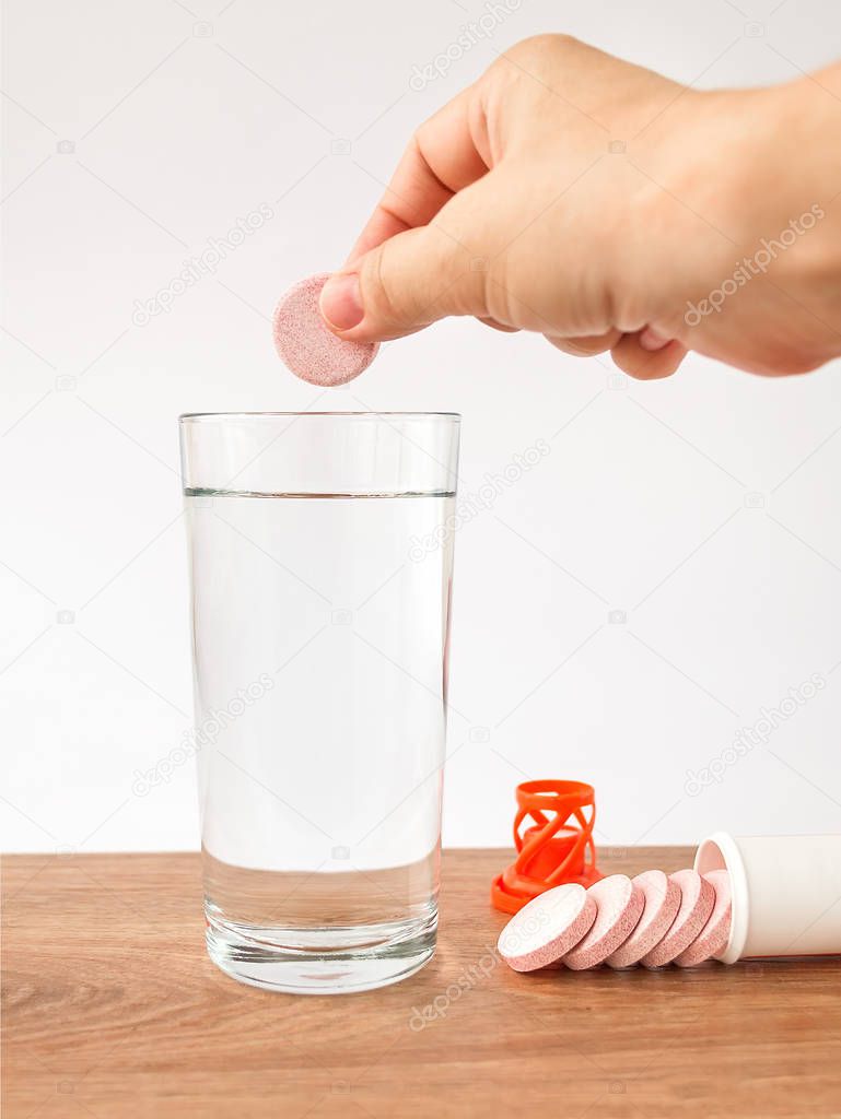 Woman hand holding soluble effervescent vitamin over a glass with water