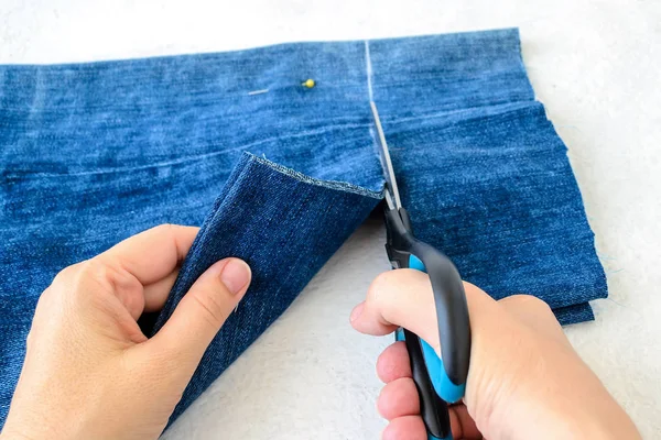 Woman hand holding a scissors and cutting out a folded in half blue jeans