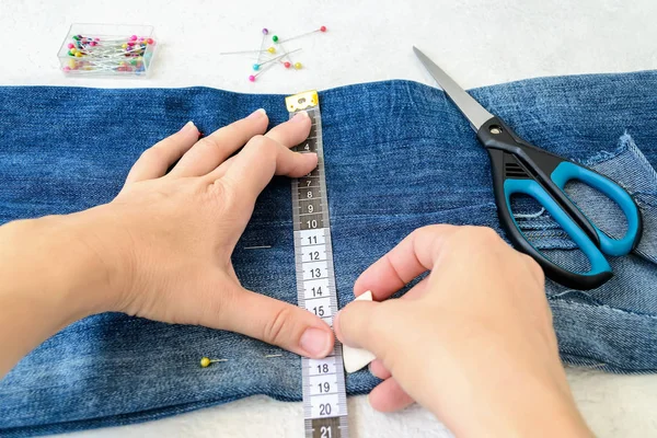 Frauenhände zeichnen eine Schnittlinie auf eine blaue Jeans. Jeans kürzen. — Stockfoto