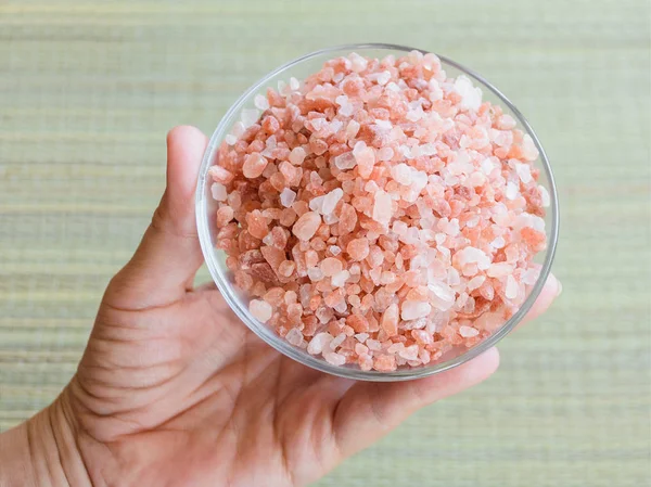 Donna mano tenendo un piattino di vetro con mucchio di sale himalayano rosa — Foto Stock