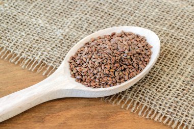 Bir çuval bezi arka plan üzerinde tahta bir kaşık tüm keten tohumu.