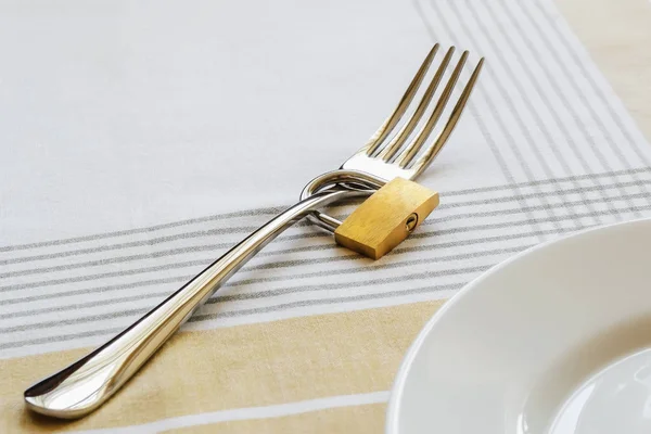 Tenedor de metal bloqueado con candado cerca de plato blanco vacío en una mesa — Foto de Stock