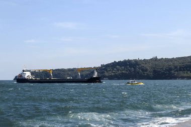 Small pilot ship leads a large black cargoship to the seaport