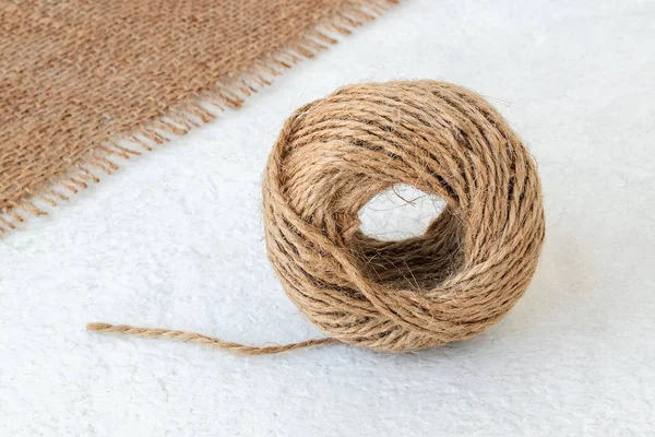 Natural hemp cord ball and burlap on a rough white surface.