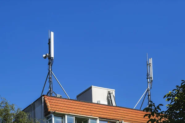 Dos antenas de comunicación celular en un tejado de azulejos naranja — Foto de Stock