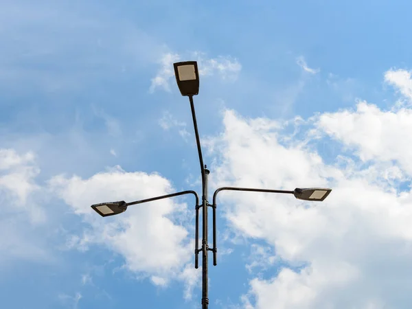 Mavi gökyüzüne karşı açık bulutlu bir direkte üç sokak lambası. Sokakları ve yolları aydınlatmak için modern enerji tasarrufu teknolojileri. Led sokak lambaları. Düşük açı görünümü.