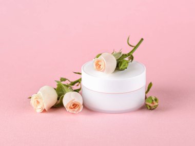 Yüz kremi ve pastel pembe arka planda açık şeftali renginde güller. Nemlendirme ve temizleme için kozmetik ürünleri. Cilt, saç veya vücut bakımı. Ön görünüm.