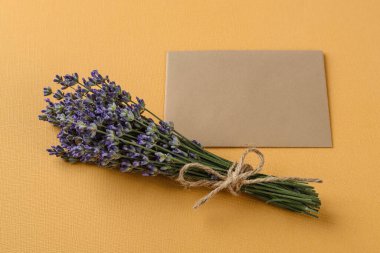 Küçük bir demet kokulu lavanta. Kalıtsal sarı arka plan üzerine notlar almak için boş bir kağıt parçasının yanında. Fotokopi alanı olan yaz ve romantik tebrik kartı. Üst görünüm.