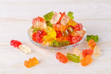 Çok renkli jelibon, beyaz ahşap masanın üzerinde cam bir tabakta şeker taşır. Farklı renkte jöle tatlılar. Meyve suyu, jelatin ve şekerden yapılan popüler jelibonlar. Ön görünüm.