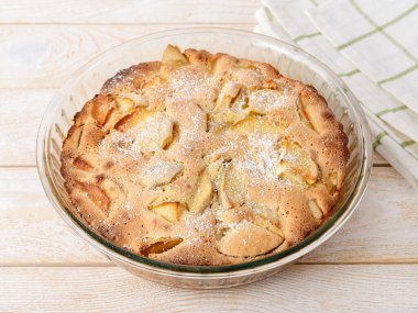 Beyaz ahşap bir masada cam bir fırında taze pişmiş tatlı ve ekşi elmalı turta. Ev yapımı tatlı pişirme için kolay bir tarif. Kahvaltılık börekler. Üst görünüm.