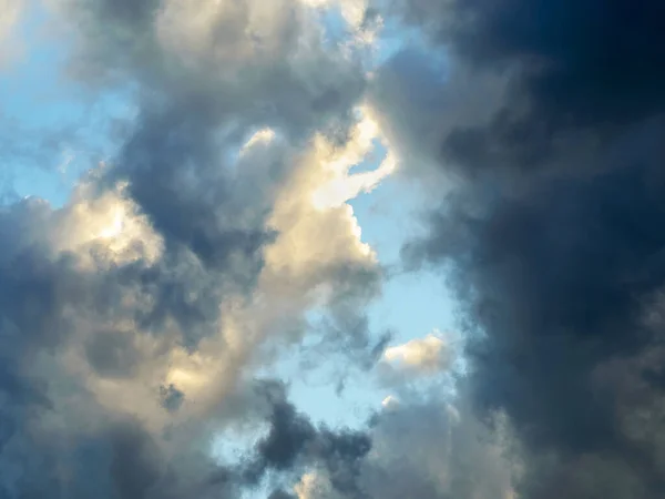 Rift in gray clouds. Bright blue sky is visible through the gap in the dark clouds. Rain clouds surround the last spot of a clear sky. Scenic skyscape.