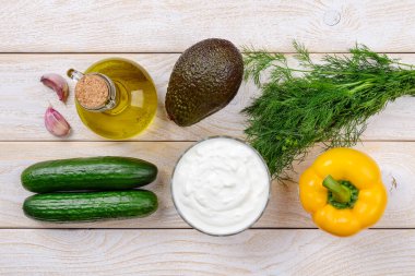Çiğ salatalık çorbası püresi: Yunan yoğurdu, salatalık, avokado, sarı dolma biber, ahşap bir masada dereotu ve sarımsak. Çiğ gıda diyeti. Üst görünüm.