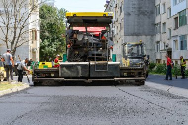 Varna, Bulgaristan, 16 Temmuz 2020. İşçiler, güneşli bir yaz gününde çok katlı bir konutun önünde yol onarımı sırasında asfalt kaldırım makinesi kullanıyorlar. Ağır makinelerin çalışması.