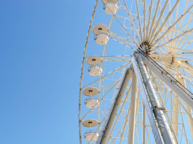 Güneşli bir yaz gününde açık mavi gökyüzüne karşı parlak beyaz ışıklarla aydınlatılmış beyaz dönme dolap çekimi. Yaz tatilinde eğlence. Düşük açı görünümü. 