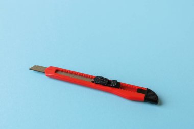 Mavi arka planda kırmızı saplı maket bıçağı. Kağıt bıçağın yerine geri çekilebilir bıçağı var. Ev ve ofis için iş gereçleri ve kırtasiye malzemeleri. Uzayı kopyala Ön görünüm.