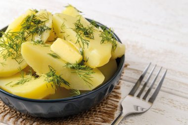 Erimiş tereyağlı haşlanmış patatesler seramik bir kâse ve beyaz ahşap bir masa üzerinde çatal ve dereotlu. Evde lezzetli sebze yemekleri pişir. Sağlıklı beslenme. Üst görünüm.