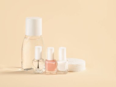 Nail varnish remover, white, pale pink and colorless nail polish, cotton pads on a powdery color background. Manicure, pedicure, nail care products. Copy space. Front view. clipart