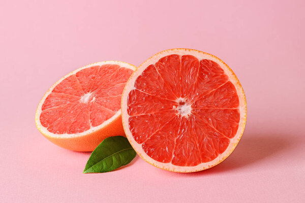 Two halves of fresh ripe juicy grapefruit and leaf on a pink background. Vegetarian, raw food diet and healthy eating. Organic antioxidant. Front view.