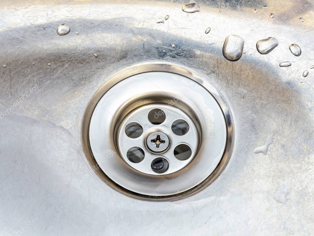 New strainer in the old metal kitchen sink with water drops. Install, clean and repair of domestic plumbing fixtures made of white pvc plastic and stainless steel. Top view.