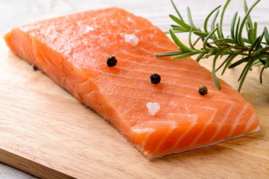 Taze çiğ somon filetosu, biber tanesi, deniz tuzu ve ahşap kesme tahtasındaki biberiye. Sağlıklı beslenme, deniz ürünleri tarifi malzemeleri ve organik omega 3 kaynak kavramları. Yakın plan..