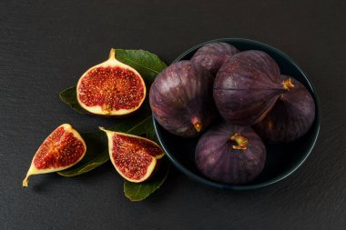 Tam ve taze taze incir meyvelerini mavi bir seramik kasede siyah bir zemin üzerinde keserek. Tatlı meyveler ve meyveler. Vejetaryen, çiğ gıda diyeti ve sağlıklı beslenme. Üst görünüm. 