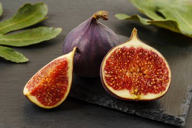 Siyah bir arkaplanda taze taze incir meyvelerinin yarısı ve dörtte biri. Tatlı meyveler ve meyveler. Vejetaryen, çiğ gıda diyeti ve sağlıklı beslenme. Üst görünüm. 