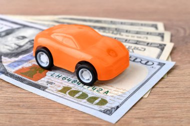 Birkaç yüz dolarlık banknotta turuncu oyuncak araba. Araba satın alma, kiralama, hizmet, onarım ve sigorta masrafları. Pahalı bir alışveriş için para biriktir. Masraflar için planlama. Ön görünüm.
