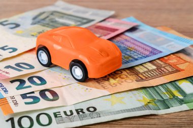 Farklı avro banknotlarında turuncu oyuncak araba. Araba satın alma, kiralama, hizmet, onarım ve sigorta masrafları. Masraflar için planlama. Ön görünüm.